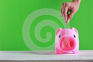 Hand putting a coin into a piggy bank on green background.