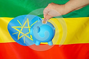 Hand putting coin to piggy bank on Ethiopia flag background
