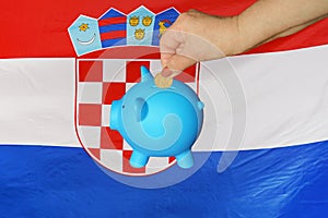 Hand putting coin to piggy bank on flag of Croatia background