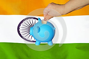 Hand putting coin to piggy bank on India flag background