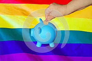 Hand putting coin to piggy bank on LGBT flag background