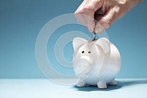 Hand putting coin into white piggy bank on blue background