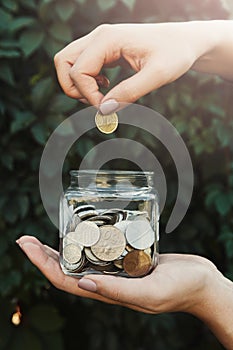 Hand putting coins in glass jar, green background