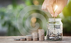 Hand putting coins in the jar on wooden table. The concept of saving money, finance, business and investment.