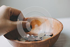 hand putting Coins in a wooden bowl, donate and give concept.