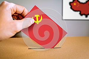 A hand putting an Communist party flag vote in the ballot box.