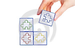 Hand putting cubes with colorful jigsaw puzzle pieces together isolated on white background. Finding solution from