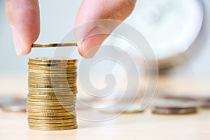 Hand putting gold coin stack with blurred clock background, Finance and investment save money concept