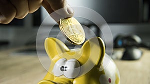 Hand putting golden bitcoin in to piggy bank money box with a computer on background. Cryptocurrency investment concept