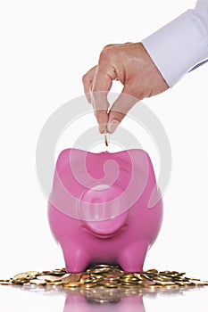 Hand Putting Money In Overflowing Piggy Bank
