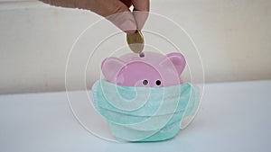 Hand putting money in pink piggy bank. piggy bank wearing protective face mask. saving money for health concept