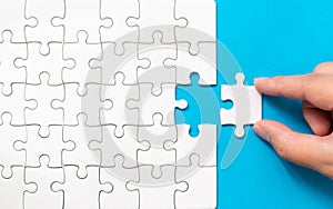 Hand putting piece of white jigsaw puzzle on blue background. Team business success partnership or teamwork