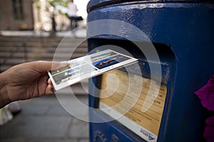 Hand putting a postcard in a Blue Guernsey Post Box unique to Guernsey in the town of St Pierre Port St Peter Port, the main