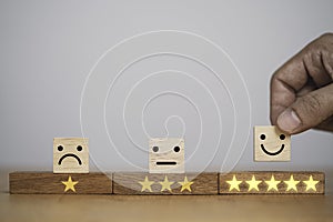 Hand putting smiley face and golden yellow stars which print screen on wooden cube block for customer survey quality of product