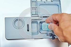 Hand putting soap tablet in the dishwasher machine, close up. Kitchen domestic appliance concept