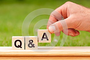 Hand putting wood block cube with alphabet Q and A on wooden table. Questions and answers concept