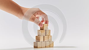 Hand putting wood cubes arranged in the pyramid shape on white