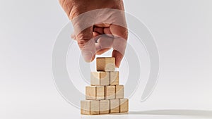 Hand putting wood cubes arranged in the pyramid shape on white