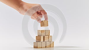 Hand putting wood cubes arranged in the pyramid shape on white