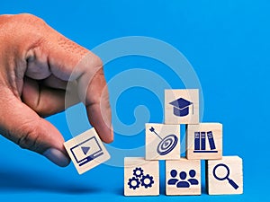 Hand putting wooden cube with e learning icons against blue background.