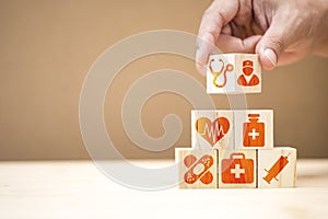 Hand putting wooden cubes stacking of healthcare medicine and hospital icon on table. Health care insurance business and