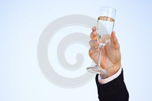 Hand raising champagne glass against clear sky