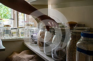 A hand reaches for a glass jar in a country kitchen pantry.