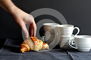 hand reaching for a croissant near stacked white coffee cups