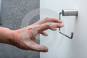 A hand reaching for an empty toilet paper holder