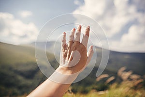 Hand reaching out to green hills in summer mountains. Summer vacation in mountains. View on top of green hills and clouds
