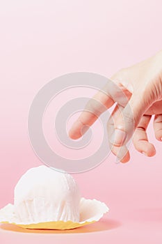 Hand reaching out to pick a delicious strawberry daifuku, Japanese rice cake up against pink background