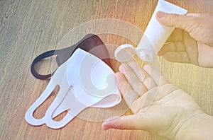 The hand receives an alcohol gel from a white tube. Mask, protection, black, white, background, wooden table