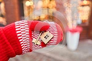 Hand in red mitten holding key with house shaped keychain. Mortgage or rent concept. Real estate, hypothec, moving home