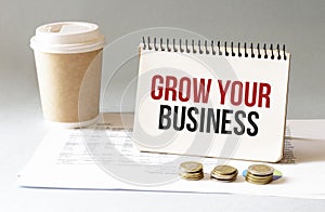 Hand with red pen. Cofee cup. Stick. Keyboard and white background. GROW YOUR BUSINESS sign in the notepad