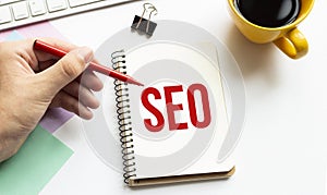 Hand with red pen. Cofee cup. Stick. Keyboard and white background. SEO sign in the notepad