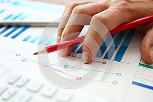 Hand with red pencil lies on comparative chart