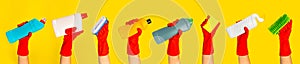 Hand with a red rubber glove holding cleaning products on a yellow background.