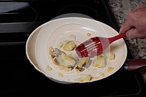 Hand with Red Spoon Cooking Boiled Potatoes in a Stovetop Pan