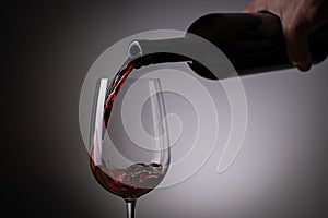 A hand red wine pouring from the bottle to the wine glass side view