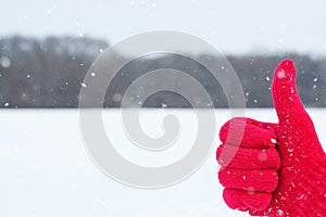 Hand in red woolen glove with thumb up on winter