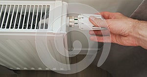 Hand reduces the temperature in the house on the thermostat of the central radiator. Close-up, top view.