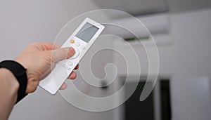 Hand with remote control is directed to air conditioner in room