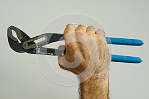 Hand of repairman holding a pipe wrench with blue handle over white background