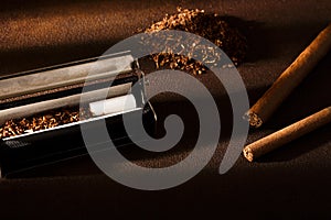 Hand-rolled cigarette, rolling machine, cigarillos, scattered tobacco on background, cigarette roll with filter, cigarette filters