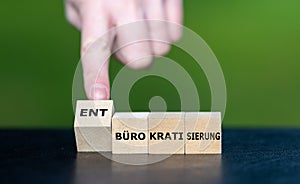 Hand rolls the cube and changes the German term (bureaucratization) to (de-bureaucratization).