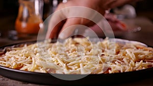 Hand rotate a pizza sprinkled with cheese in baking pan