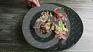 Hand rotates black plate with roasted meat pieces, potato chips, and vegetable salad