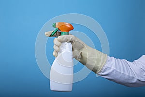 Hand with rubber glove holding a white spray bottle on blue background