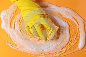 A hand in a rubber glove holds a cleaning sponge with foam on a bright yellow background. household chores and cleaning concept