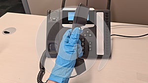Hand in rubber glove holds a handset over modern phone in the office